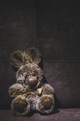 Cute plush brown bunny toy sits on a suede sofa, the image will appeal to young children.