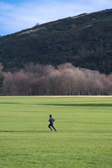 Obraz premium Young runner is busy jogging in the green field on the background of a big mountain
