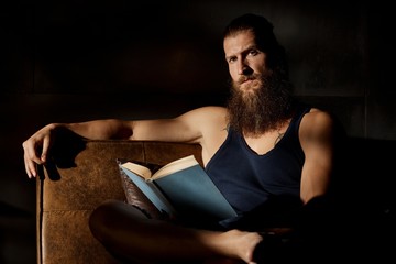 Young bearded man sitting in dark room with book
