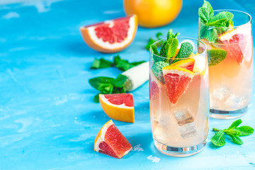 Grapefruit and fresh mint cocktail with juice, cold summer citrus refreshing drink gin tonic cocktail or beverage with ice on blue concrete surface