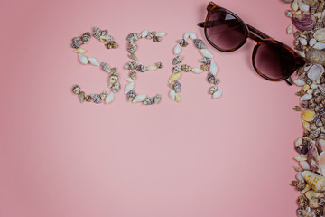 Sunglasses and the word sea lined with seashells on a pink background. Tourism concept