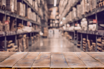 Empty wooden table on defocused blurred boxes on rows of shelves.