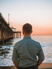 A blond man in a shirt is posing near the Manhattan beach pier in Los Angeles at sunrise