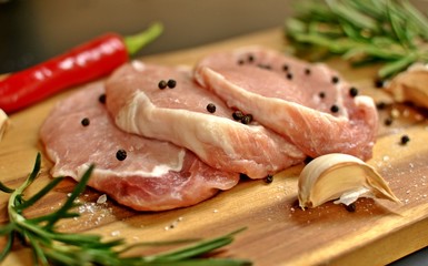 Raw fresh uncooked sliced pork meat fillet dish with rosemary, pepper, red chili pepper, garlic on wooden board and black background.