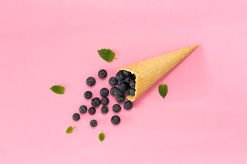 Freshly blueberries in an ice cream cone on a pink background. Blueberry explosion. Summer refreshment concept. Flat lay, top view. Natural Organic Food Style.