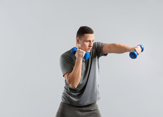 Sporty young man training with dumbbells against grey background