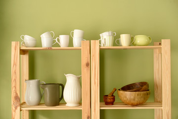 Set of clean dishes on wooden shelves near color wall