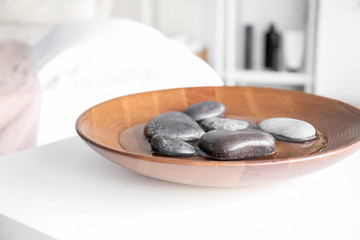 Plate with water and massage stones on table in spa salon