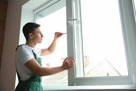 Young worker repairing window in flat
