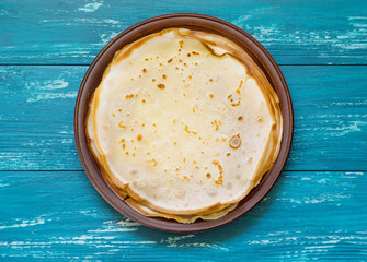 Russian pancakes on a clay plate on an azure table.Top view