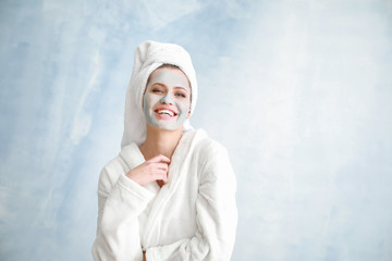 Beautiful young woman with facial mask on light background