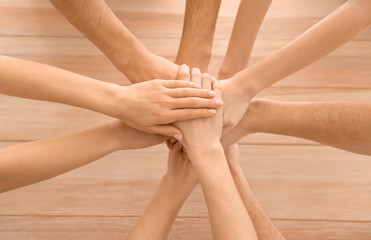 Team of young volunteers putting hands together at wooden table
