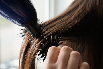 Hairdresser with blow drier brushing long hair of young woman in salon, closeup