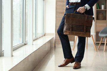 Fashionable young man with bag near window