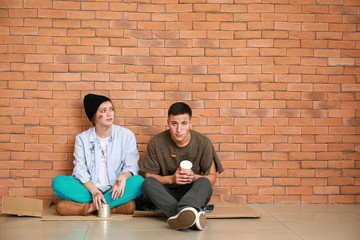 Poor homeless people sitting near brick wall