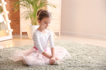 Young ballerina girl sitting on carpet adjusting ballet slipper, childhood dance training and artistic development © Pixel-Shot