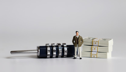 A miniature man standing with a combination lock and wad of bills.