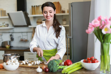 Beautiful woman cutting mushrooms in kitchen at home