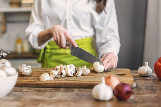 Beautiful woman cutting mushrooms in kitchen at home