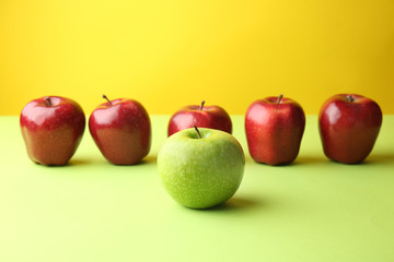 Green apple among red ones on color background. Concept of uniqueness