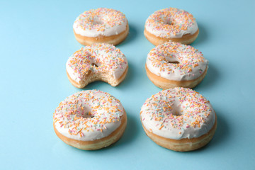 Bitten doughnut among whole ones on color background. Concept of uniqueness