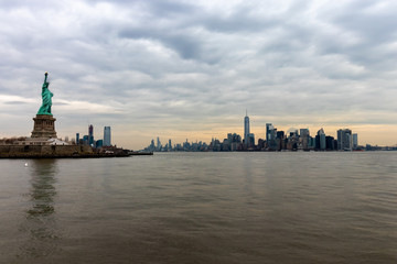 View of New York City skyline and Statue of Liberty with dramatic sky at dusk, New York, USA