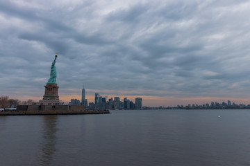 Fototapeta premium View of New York City skyline and Statue of Liberty with dramatic sky at dusk, New York, USA