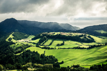Naklejka premium Beautiful landscape of Azores islands, Sao Miguel. A lot of green fields separated with trees between each other. Cloudy sky.