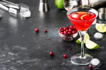 Classic alcoholic cocktail cosmopolitan with vodka, liqueur, cranberry juice, lime, ice and orange zest, gray bar counter background, bartender tols, space for text