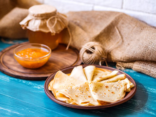 Russian pancakes on a wooden plate on an azure table with honey and apricot jam. Food still life