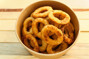 Cardboard bowl with tasty onion rings on wooden table