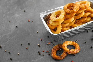 Takeaway box with tasty onion rings on grey table