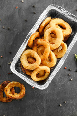 Takeaway box with tasty onion rings on grey table