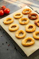 Cooling rack with tasty onion rings on grey background