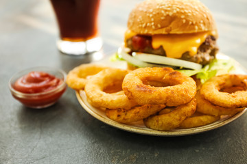 Plate with tasty burger and onion rings on table
