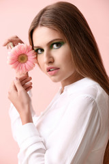 Beautiful young woman with bright makeup and flower on color background