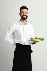 Handsome waiter with fresh salad on light background