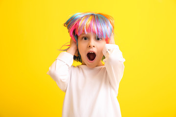 Shocked little girl in bright wig on color background