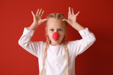 Funny little girl with clown nose on color background. April fools' day celebration
