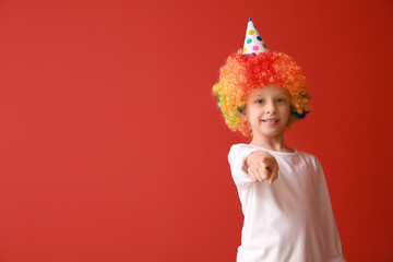 Funny little girl in bright wig pointing at viewer on color background. April fools' day celebration