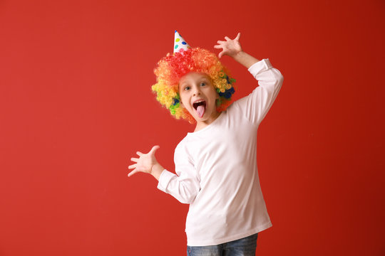 Funny little girl in bright wig on color background. April fools' day celebration