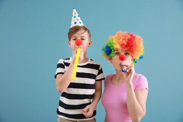 Little boy and his mother in funny disguise with party whistles on color background. April fools' day celebration