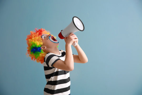 Cute little boy with clown makeup and megaphone on color background. April fools' day celebration