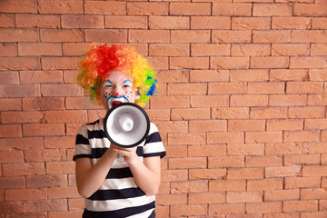 Cute little boy with clown makeup and megaphone against brick wall. April fools' day celebration