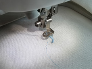 A needle of the computer embroidery machine with a light blue thread in the process of embroidery,...