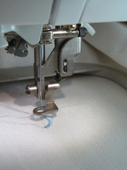 Mechanism with a needle of the computer embroidery machine, close-up. The process of embroidering a light blue pattern on a white textured fabric tucked into the hoop