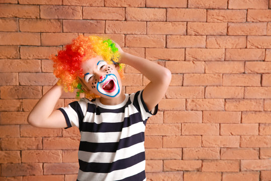 Cute little boy with clown makeup against brick wall. April fools' day celebration
