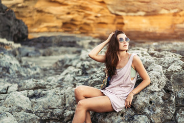 Pretty long hair brunette tourist girl relaxing on the stones near sea.