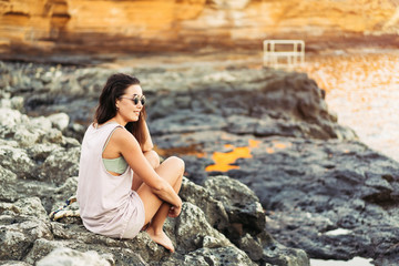Pretty long hair brunette tourist girl relaxing on the stones near sea.