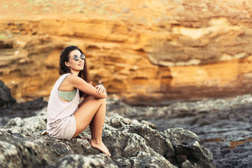 Pretty long hair brunette tourist girl relaxing on the stones near sea.